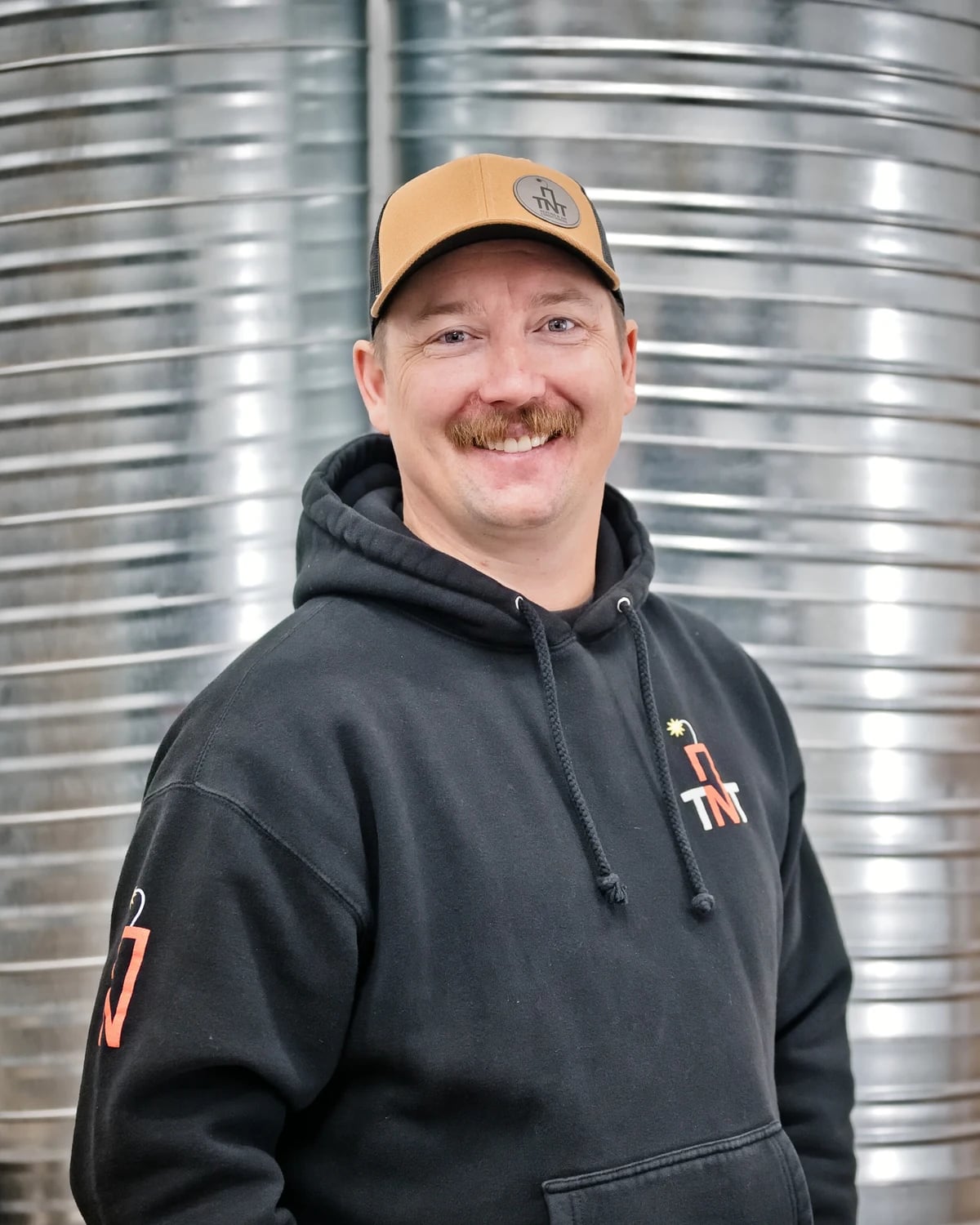 AC installation Calgary: one of the TNT owners in a TNT hoodie, in front of spiral duct in the Calgary shop