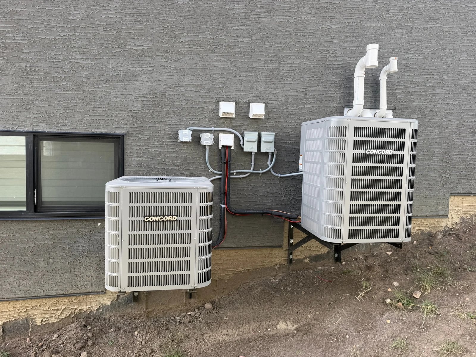 Two Concord air conditioners on wall brackets beside a Calgary home with the line sets run into the wall