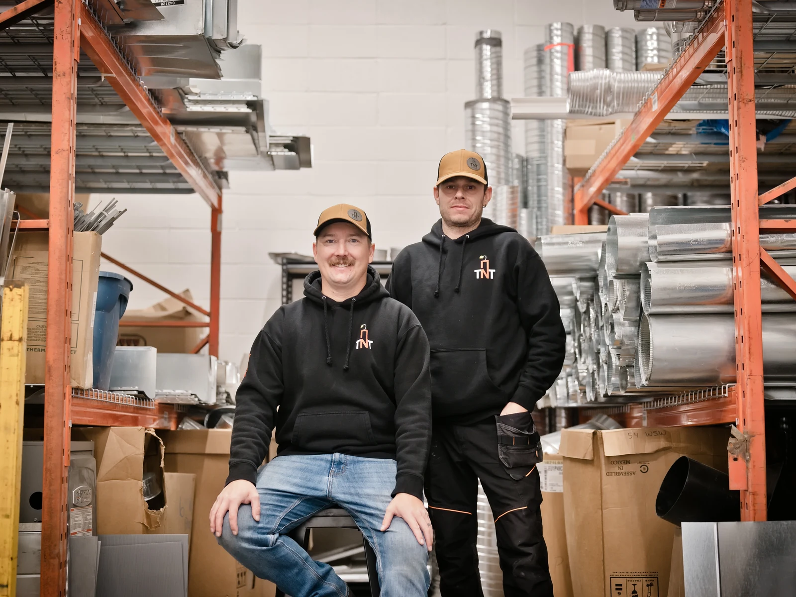 Calgary HVAC contractor: the two owners of TNT Heating in their southeast Calgary shop, among duct and sheet metal stock